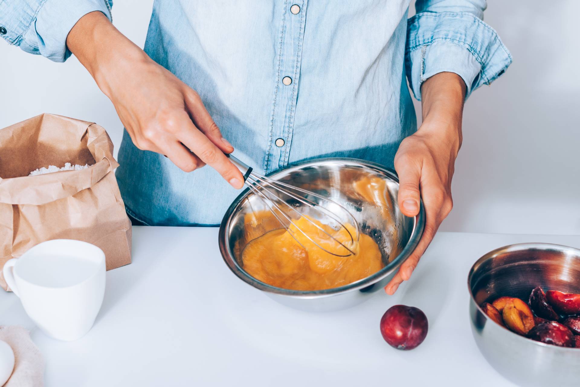 female's hands whisk eggs with sugar to bake fruit pie