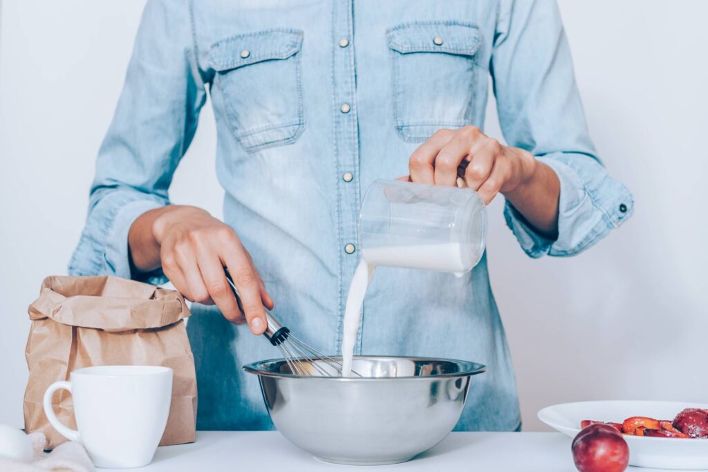 Young woman cooking plum cake, whisking dough standing at table
